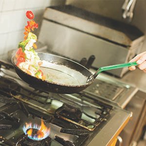 chef cooking and flipping veggies on a steel frypan.