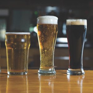 various sizes of beer in glasses sitting on a wood bar table