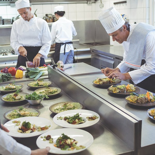chefs-working-on-a-work-table-in-the-restaurant-kitchen Paltes of food sitting on a work table while chef puts final touches on.