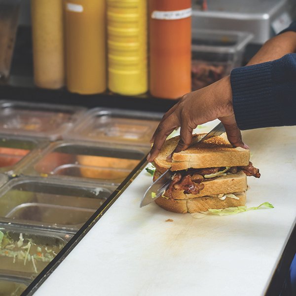 worker-cutting-sandwich-on-prep-station Worker cutting sandwich on prep station in restaurant.